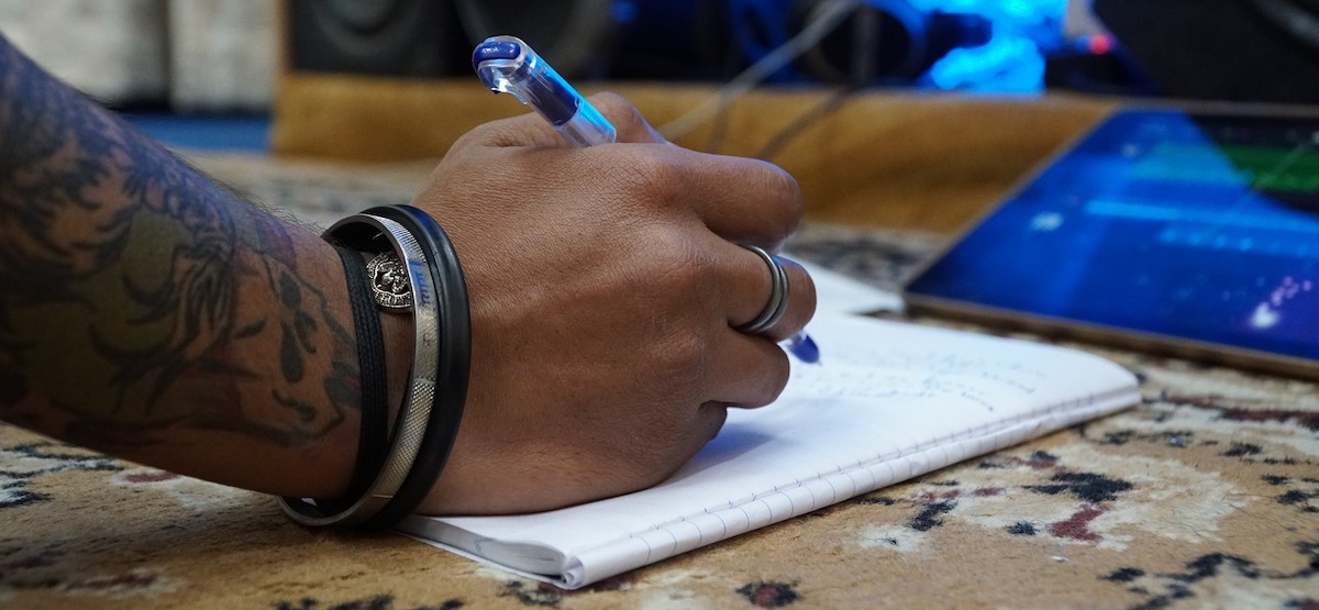 song writing. Tattooed man's arm writing lyrics on paper