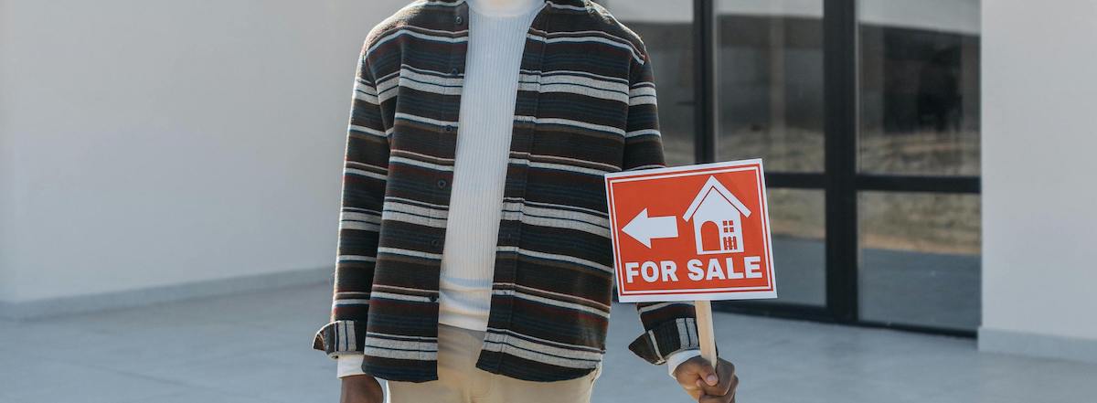 Man holding for sale sign in front of new house
